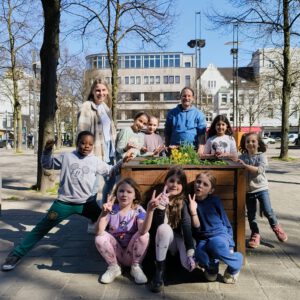Gruppenbild einer Gruppe Kinder, die um ein Hochbeet mit neu gepflanzten Blumen stehen und in die Kamera schauen.